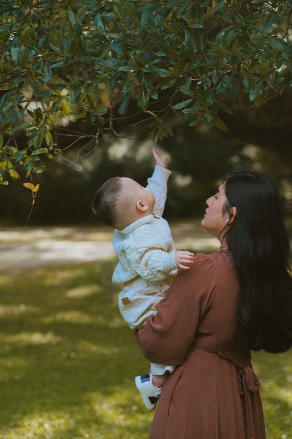 A mother holding her child up toward a tree branch